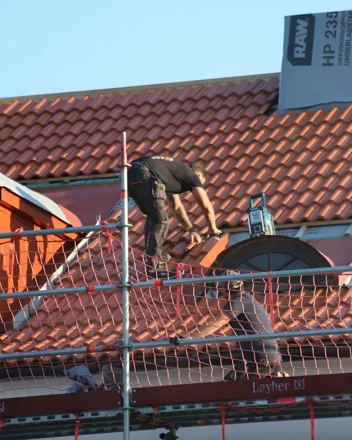 Couvreur posant des tuiles sur un toit, derrière l'échafaudage du chantier